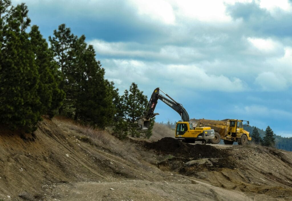 Current image: Excavator and truck working at a construction site in Coeur d'Alene, Idaho with cloudy skies.