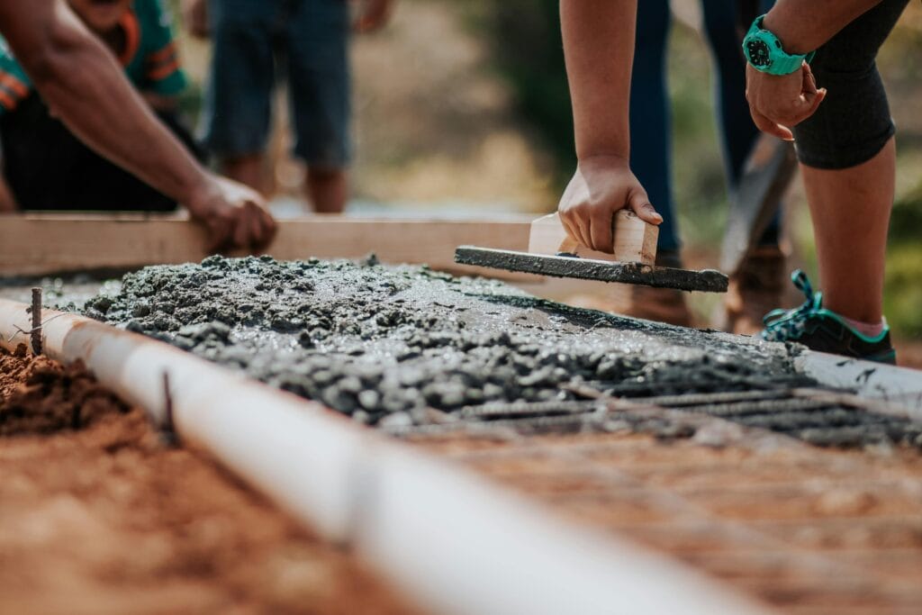Current image: Construction workers leveling fresh cement on a sunny day at an outdoor site.
