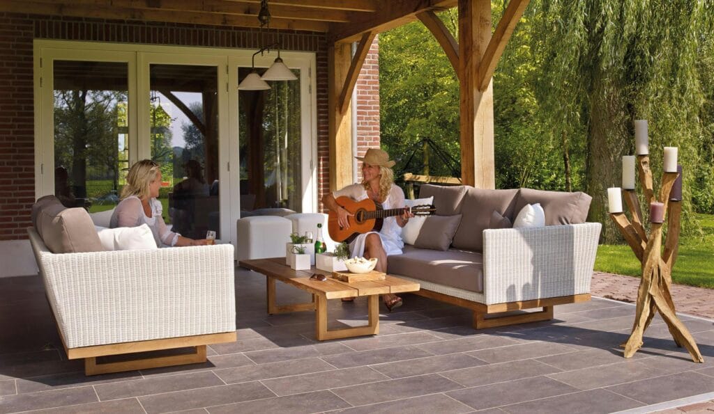 Current image: Two women enjoying a serene patio scene with a guitar and candles, surrounded by greenery.
